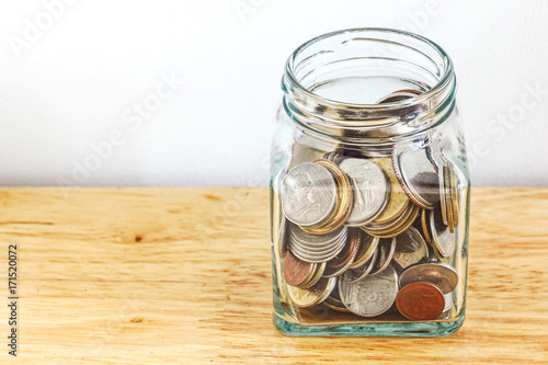 Silver and gold coin in glass jar bottle on wood table with white background