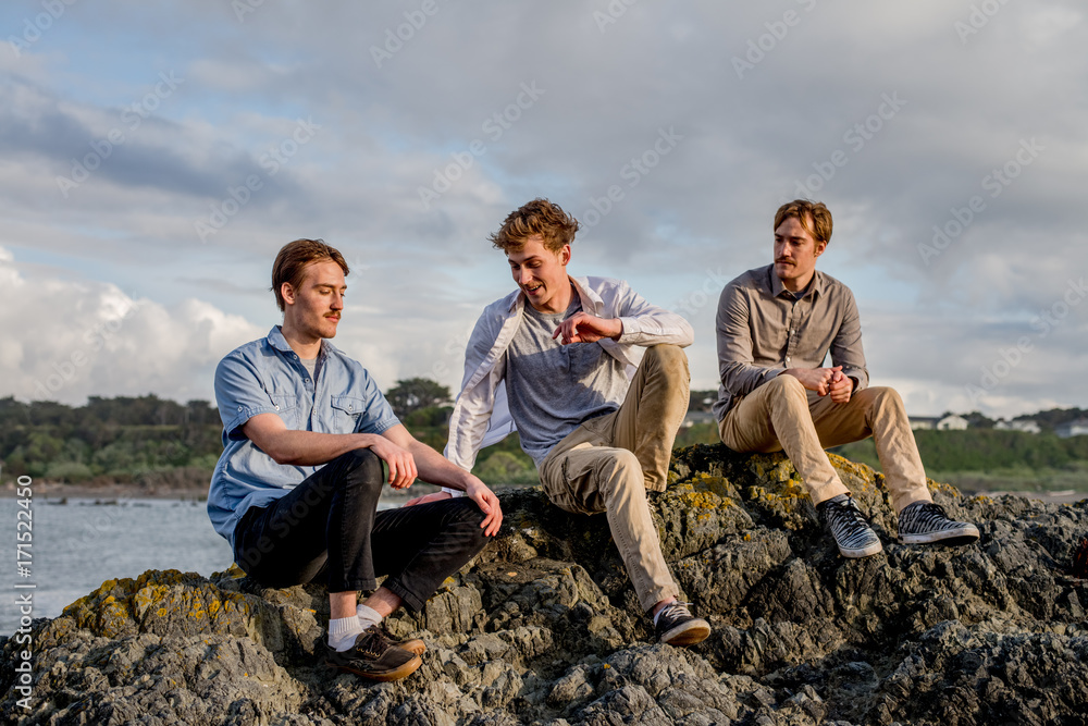 Three young men sitting on a rock by the beach
