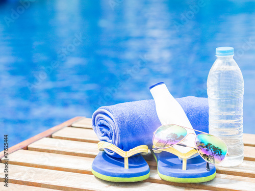 flip flops, sunglasses, blue towel and sunscreen at the side of swimming pool. Vacation, beach, summer travel concept