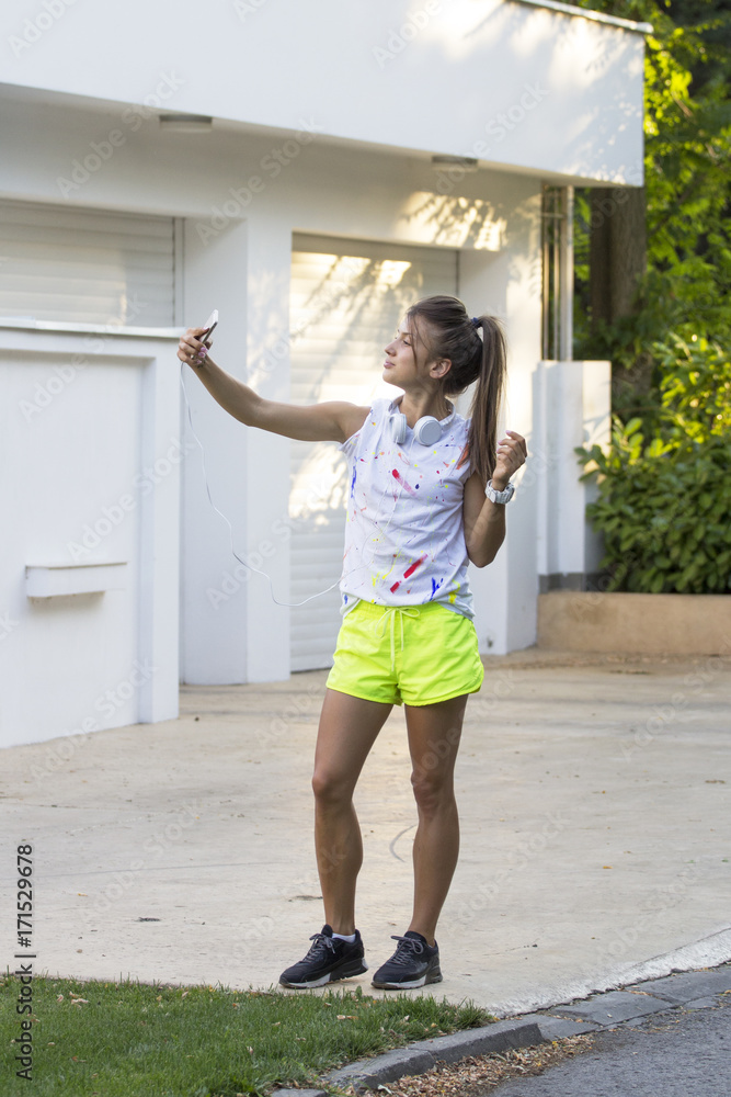 Young girl with headphones on her head resting after jogging and taking selfie by mobile phone Young girl with headphones on her head resting after jogging and taking selfie by mobile phone