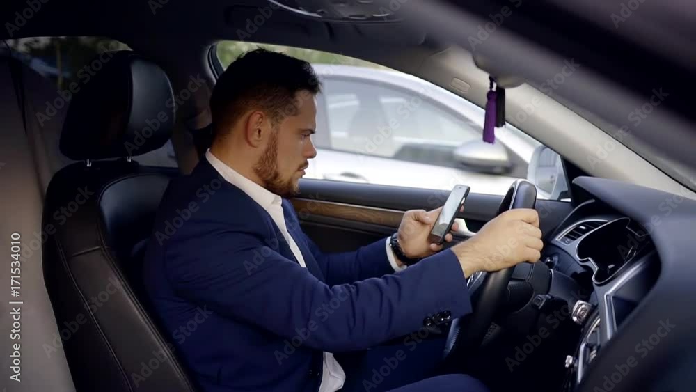 A young manager who sits in the car looks at a smartphone monitor that is connected to a WiFi A young manager who sits in the car looks at a smartphone monitor that is connected to a WiFi