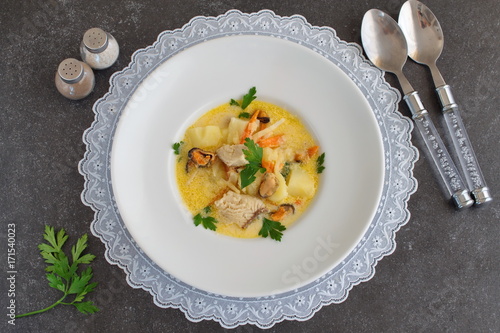 Creamy soup with fish fillet and mussles in a white plate on a white cloth on a grey abstract background. Healthy eating concept. Meditteranian lifestyle. photo