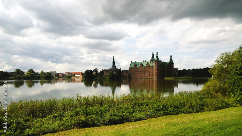 Frederiksborg castle in the suburbs of Copenhagen Hillerød. In the frame the castle, the pond next to it and a beautiful bright lawn in the foreground