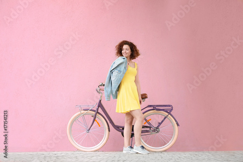 Fototapeta Naklejka Na Ścianę i Meble -  Beautiful young woman with bicycle on color wall background