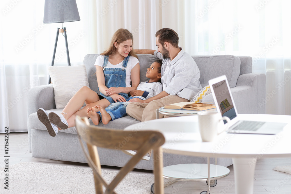 Happy couple with adopted African-American boy sitting on couch at home Happy couple with adopted African-American boy sitting on couch at home