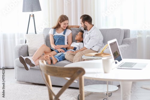 Happy couple with adopted African-American boy sitting on couch at home