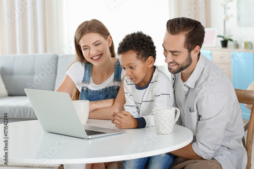 Happy couple with adopted African-American boy using laptop in living room