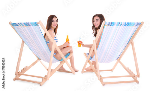 Beautiful young women with alcoholic drinks sitting on deck chairs against white background © Africa Studio