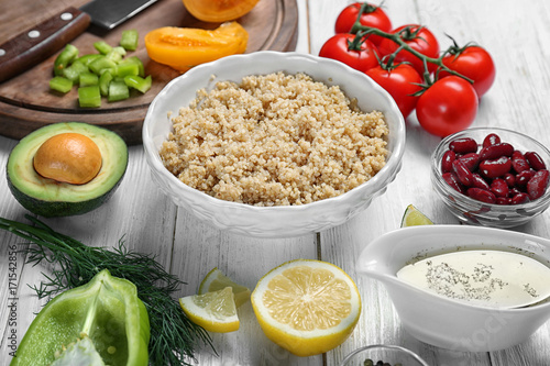 Composition with cooked quinoa and fresh products on white wooden background