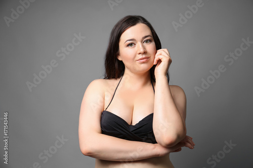 Beautiful overweight woman in black bikini on grey background