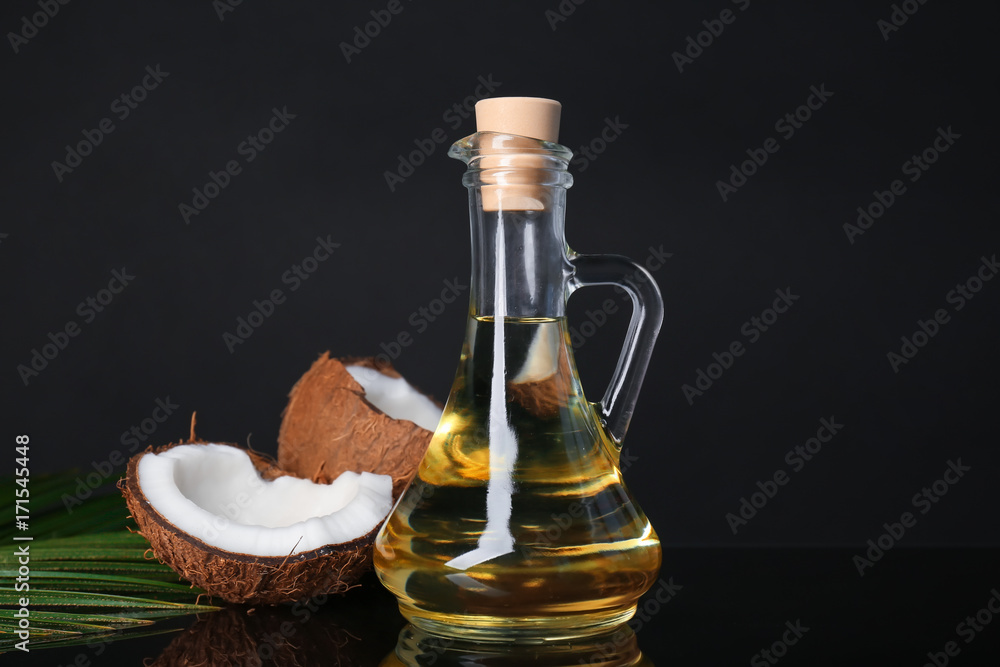 Ripe coconut and pitcher with oil on black background Ripe coconut and pitcher with oil on black background