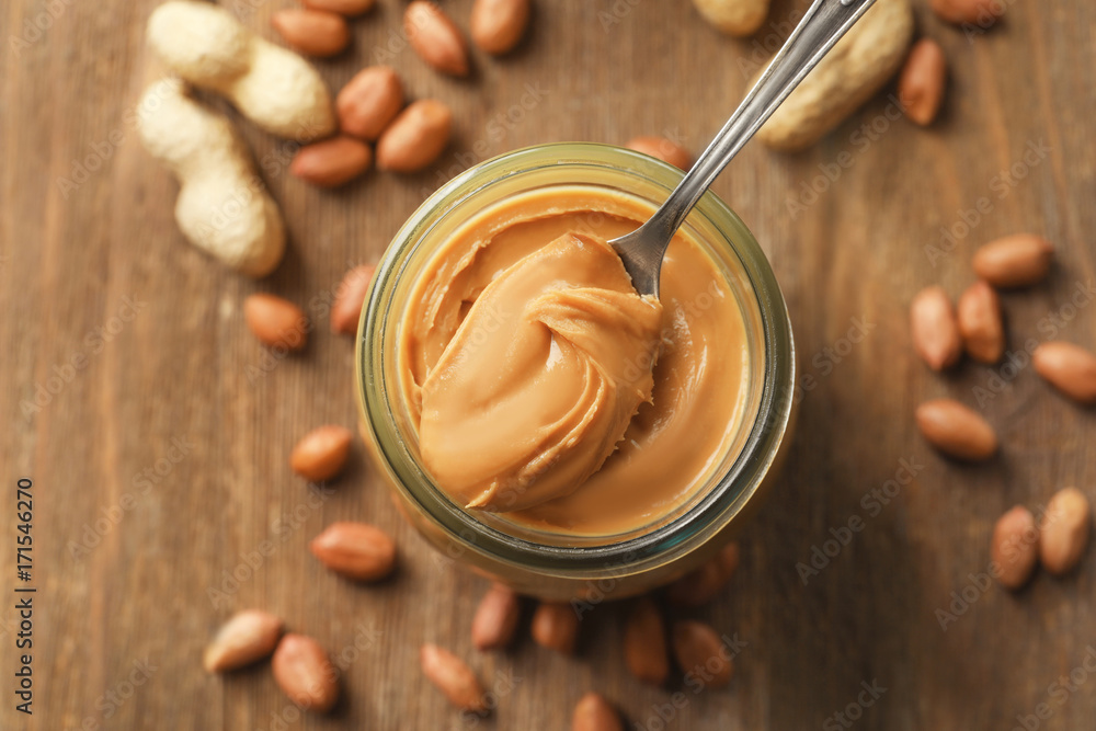 Spoon and glass jar with creamy peanut butter on kitchen table Spoon and glass jar with creamy peanut butter on kitchen table