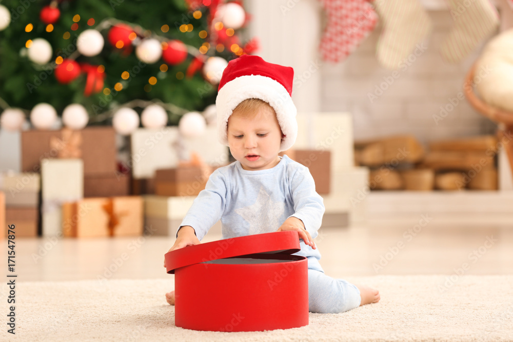 Cute little baby with giftbox in room decorated for Christmas Cute little baby with giftbox in room decorated for Christmas
