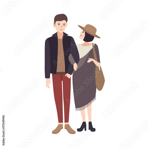 Young woman wearing fashionable poncho and hat standing beside smiling man, holding his arm and warmly looking at him