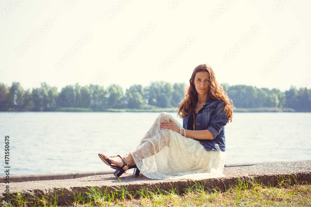 Mature woman with long curly hair wear long lace skirt and jeans jacket walk in city park. Lady relax after hard work week
