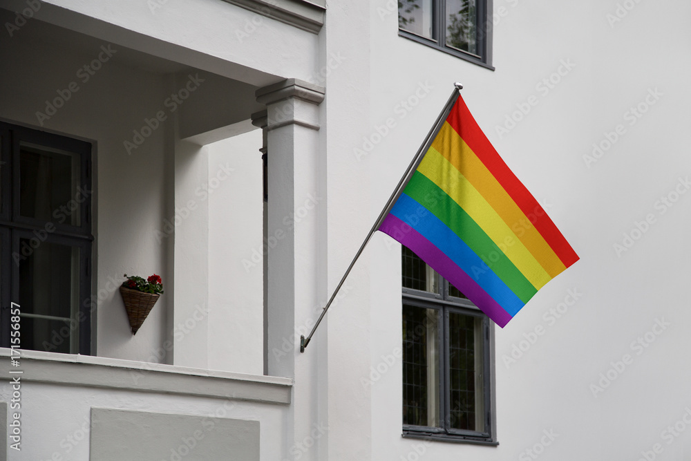 Rainbow flag. LGBT (Lesbian, Gay, Bisexual, Transgender) movement flag displaying on a pole in front of the house and waving on a home, hanging from a pole on a front door of a building.