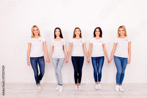 Life after fighting breast cancer exist. Carefree, international, cured, cheerful five girls are holding each other`s arms, walking to new life together, with pink ribbons symbols on chest