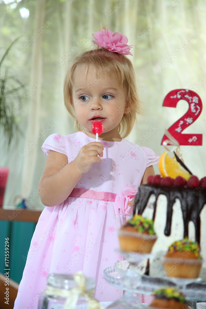 Girl birthday. A little white-haired girl of two years is trying a birthday cake. Little girl celebrating second birthday. Girl birthday. A little white-haired girl of two years is trying a birthday cake. Little girl celebrating second birthday.