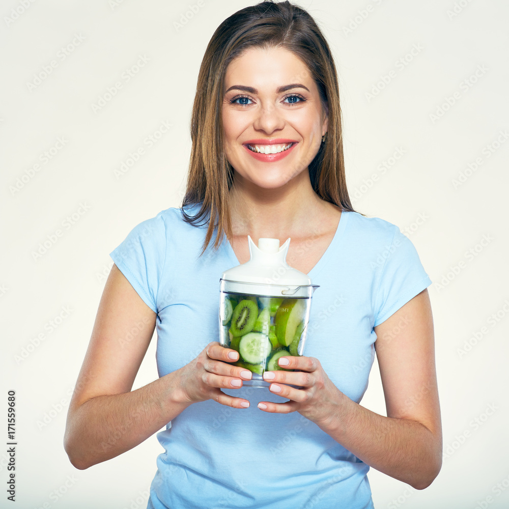 Smiling woman holding green ingredients for smoothie in blender.