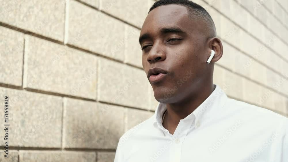 Close up of smiling handsome young businessman using smartphone. African american man talking on the phone using wireless earphones. Series of business people - interns, financial advisors, CEO Close up of smiling handsome young businessman using smartphone. African american man talking on the phone using wireless earphones. Series of business people - interns, financial advisors, CEO