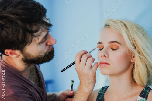 professional male makeup artist working with beautiful young blonde woman