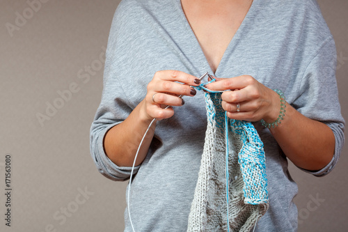 close-up of a young woman in a gray cardigan with deep cuts knits with natural gray thread blue-gray sweater at home on a gray wall background