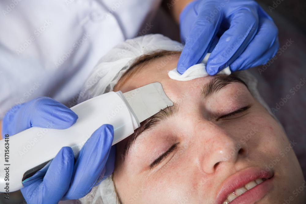 Fototapeta premium A close-up of the beautician makes a face cleaning in blue medical gloves to a girl with a problem skin, an outgoing facial treatment for cleansing the skin