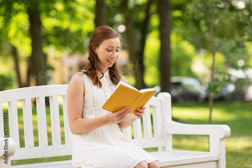 smiling young woman reading book at summer park