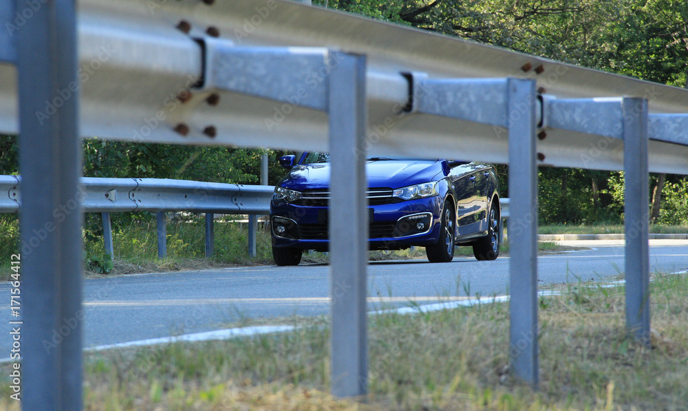 Highway railings fenced asphalt road and blue sedan on the road
Highway railings fenced asphalt road and blue sedan on the road