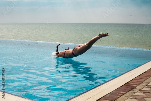 Woman jumping in a pool with ocean view
