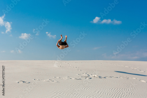 Young man jumping on the beach with white sand and bright blue sky