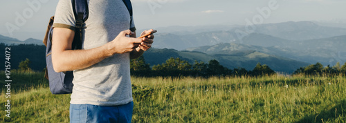 Traveler Man's hand is holding mobile phone with backpcak against mountains, space for text