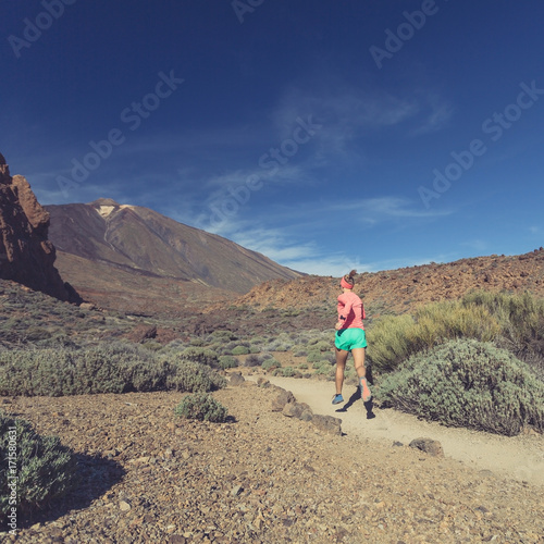 Young woman trail running in mountains on sunny day