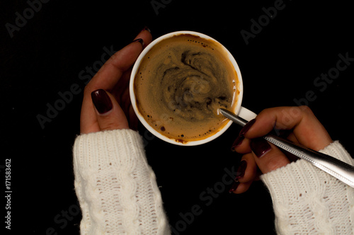 women's hands in a warm white sweater with a manicure hold a small white cup with coffee and a foam, Cozy mood