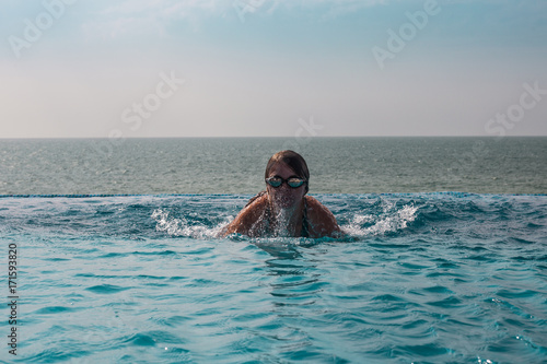 Girl in glasses in a swimming pool with ocean view