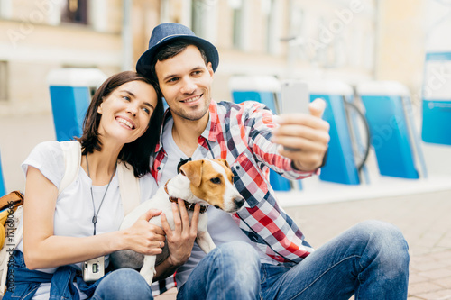 Portrait of cheerful young good looking woman leaning at her handsome husband, smiling joyfully into camera while posing for selfie. Family members travelling together, photographing themselves photo