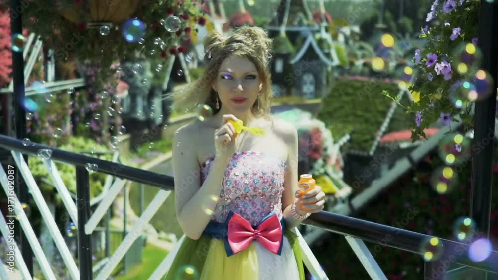 Sexy young blonde woman blowing soap bubbles in flower garden. Pretty dreaming cute girl in funny lace dress relaxes, enjoys, have fun, falling in love, among the flowers. Happy face. Slow motion