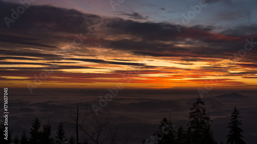 Strong orange sunset over landscapes hidden under fog.