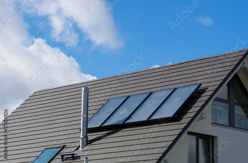 Photovoltaics on new build house roof with blue sky and aluminium chimney