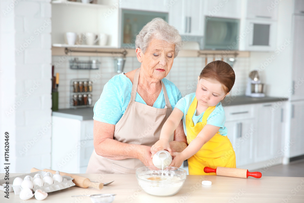 Cute little girl and her grandmother cooking on kitchen