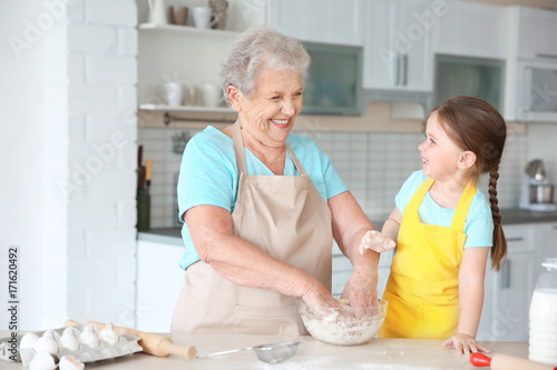 Konstfotografi Cute little girl and her grandmother cooking on kitchen