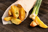 Delicious baked potato wedges in a paper cone on wooden background