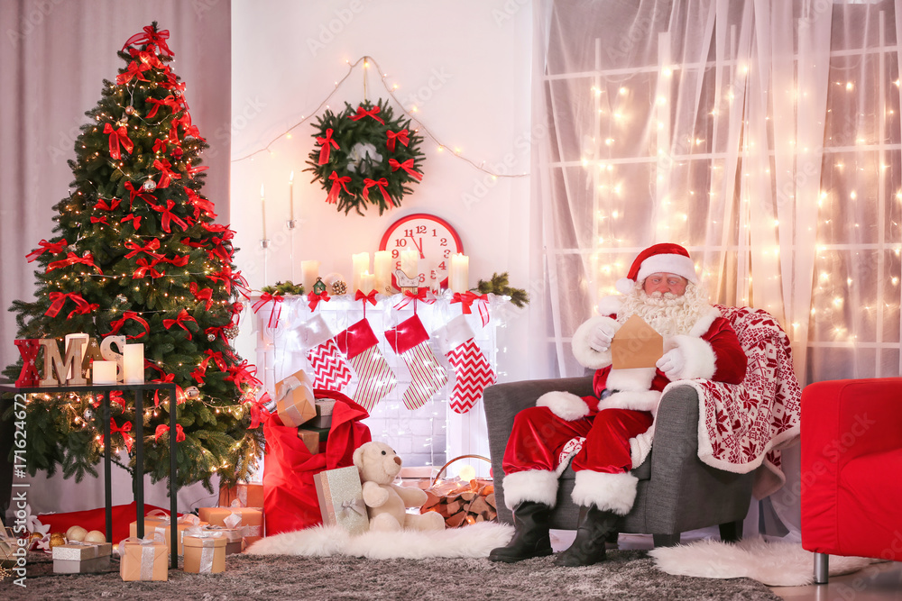 Authentic Santa Claus with letter sitting in armchair at room decorated for Christmas Authentic Santa Claus with letter sitting in armchair at room decorated for Christmas