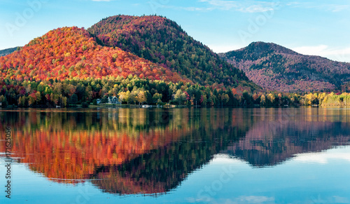 The hills covered with red maple forests are reflected in a lake in Quebec on a beautiful autumn evening