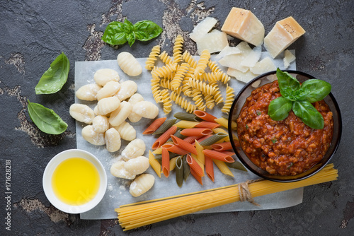 Bowl of freshly made bolognese sauce with different types of raw pasta and gnocchi, parmesan, olive oil and basil leaves