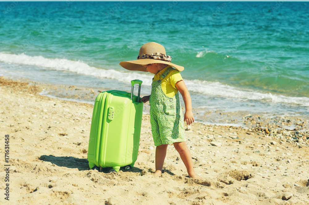 the child on the seashore with a suitcase and wearing a straw hat the child on the seashore with a suitcase and wearing a straw hat