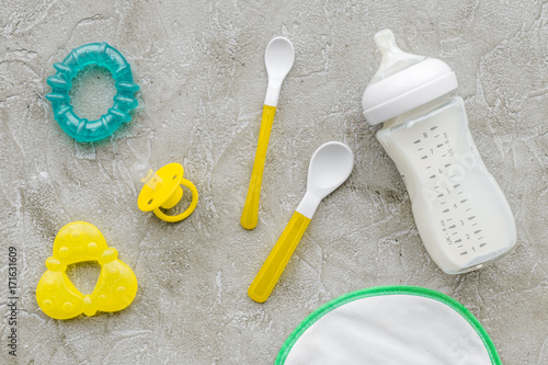 bottle with breastmilk and infant formula powdered healthy food  toys and bib on stone background top view