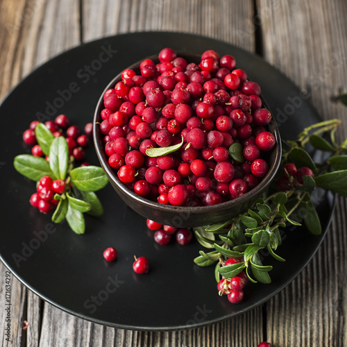 Wall Mural Fresh ripe forest northern cranberries or cowberry, lingonberry in ceramic cups of different size and color on a gray stone aged background for the concept of organic natural healthy food