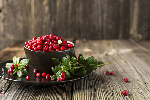 Bilde på lerret Fresh ripe forest northern cranberries or cowberry, lingonberry in ceramic cups of different size and color on a gray stone aged background for the concept of organic natural healthy food