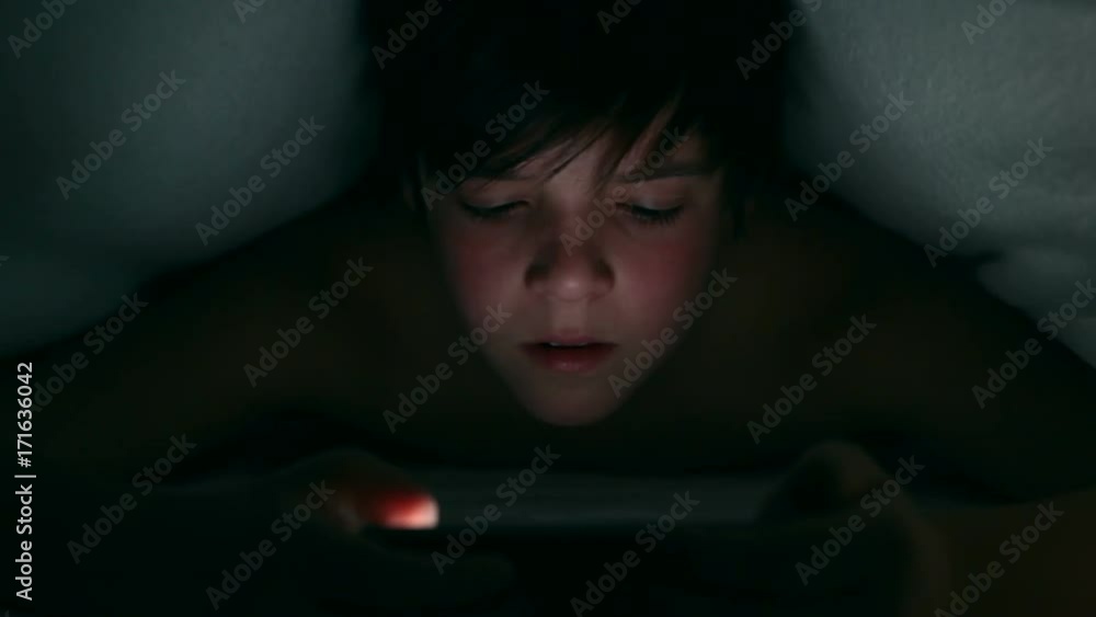 Boy browsing digital content using his smartphone under the blanket at night - closeup Boy browsing digital content using his smartphone under the blanket at night - closeup